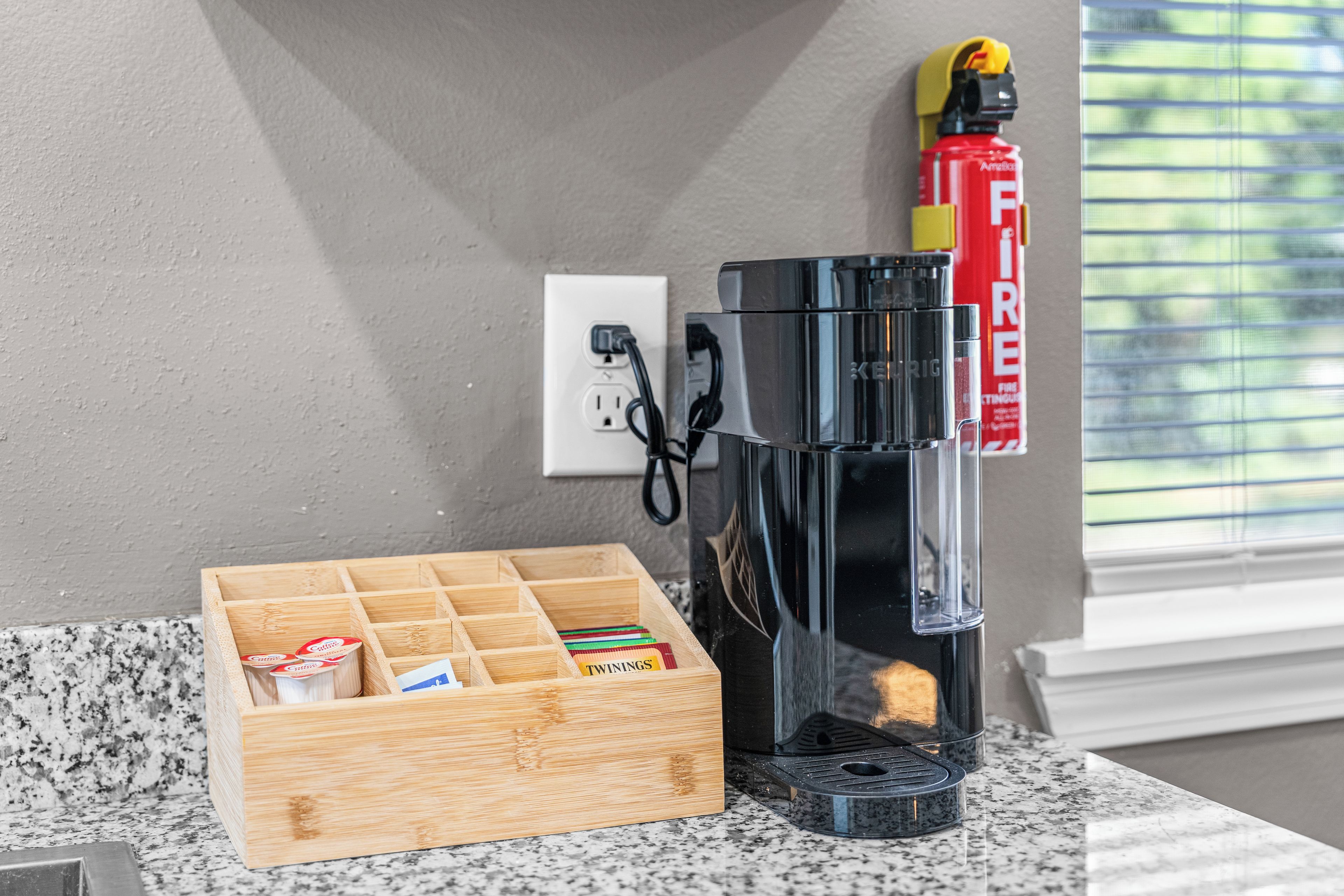 A coffee maker on a countertop, a wooden storage box with coffee pods, and a fire extinguisher on the wall.