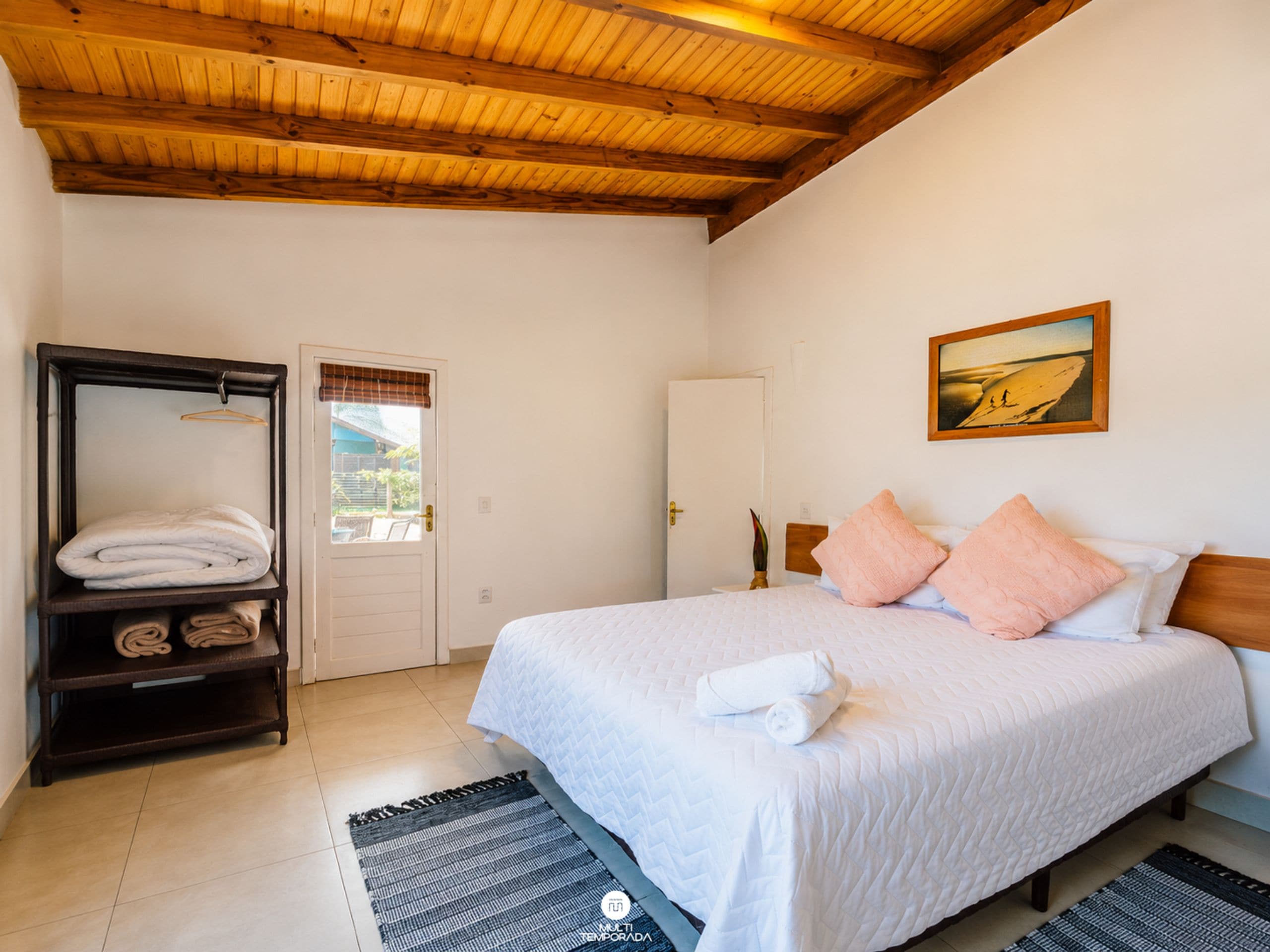 Quarto com cama, guarda-roupa, porta e um quadro na parede.