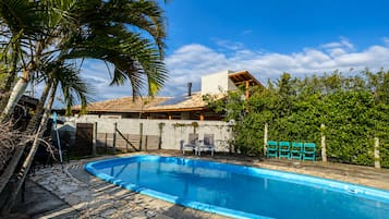 Una piscina con cubierta de piedra, rodeada de palmeras y una casa con techo de tejas.