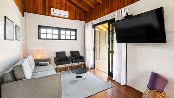 Uma sala de estar moderna com sofá, duas poltronas, mesa de centro, TV de tela plana fixada na parede e teto de madeira.