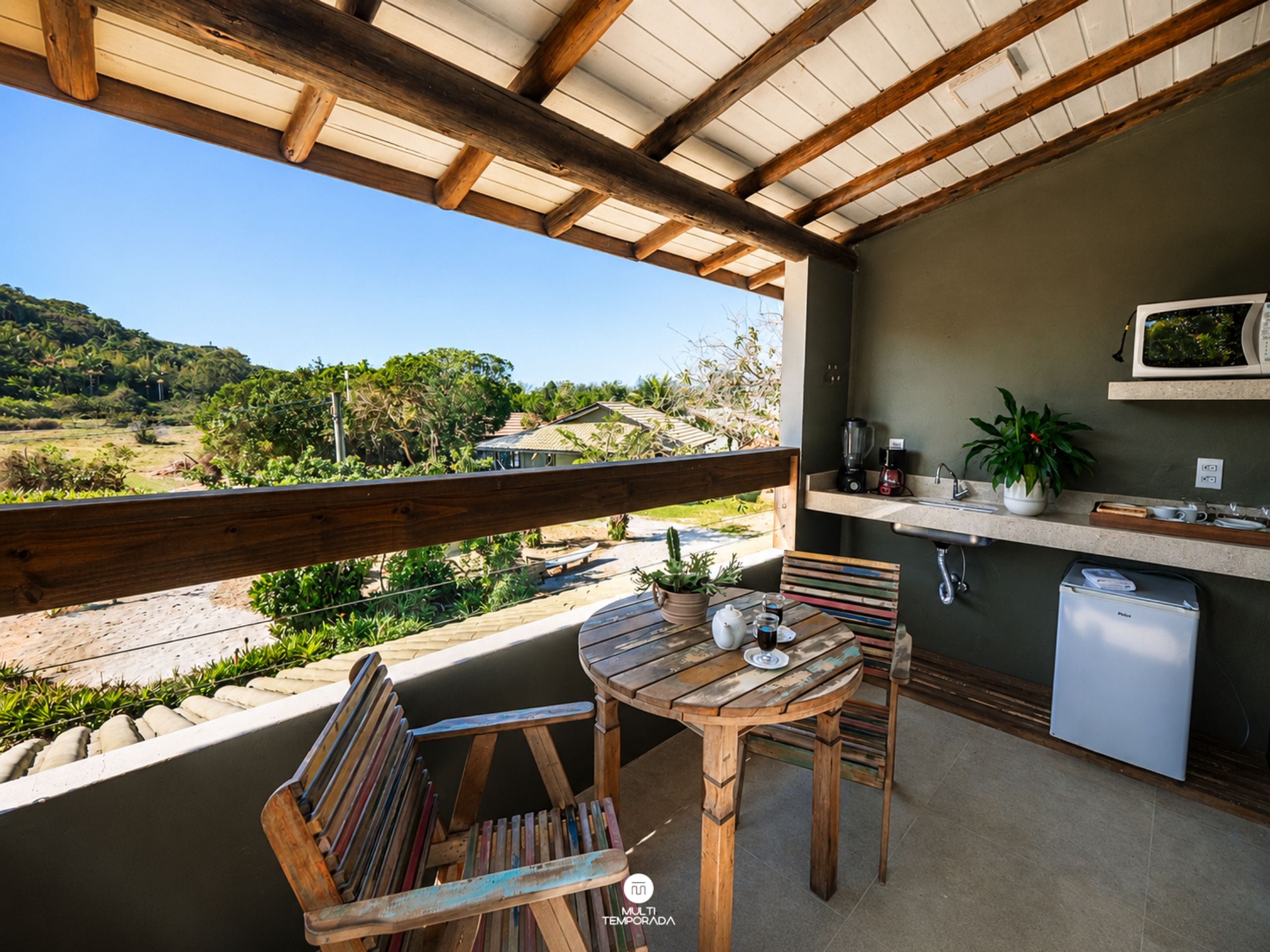 Um deck de madeira com mesa e cadeiras, uma pequena cozinha com micro-ondas e vista para a paisagem natural.