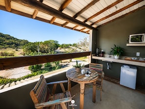 A wooden deck with a table and chairs, a small kitchen area with a microwave, and a view of a natural landscape.