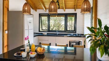 Una cocina con encimera negra, techo de madera y tres lámparas de mimbre colgantes.