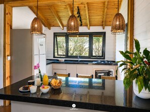 A kitchen with a black countertop, wooden ceiling, and three hanging wicker light fixtures.