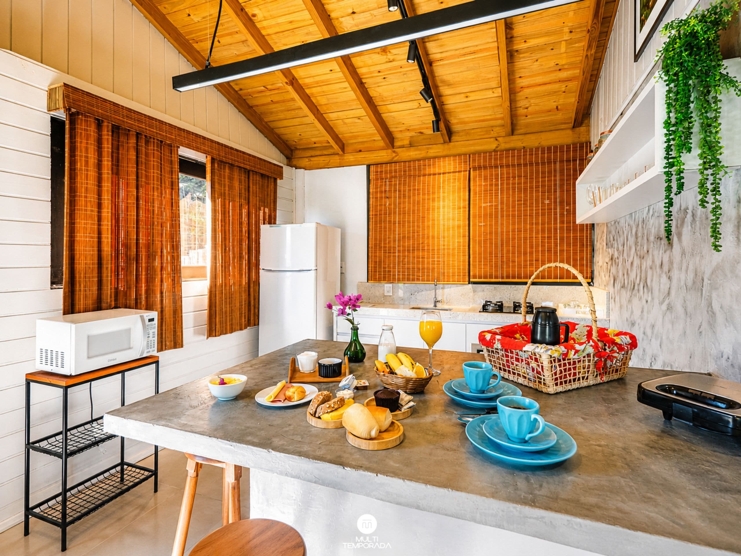 A modern kitchen with wooden cabinets, a central island with breakfast items, a microwave, and a refrigerator.