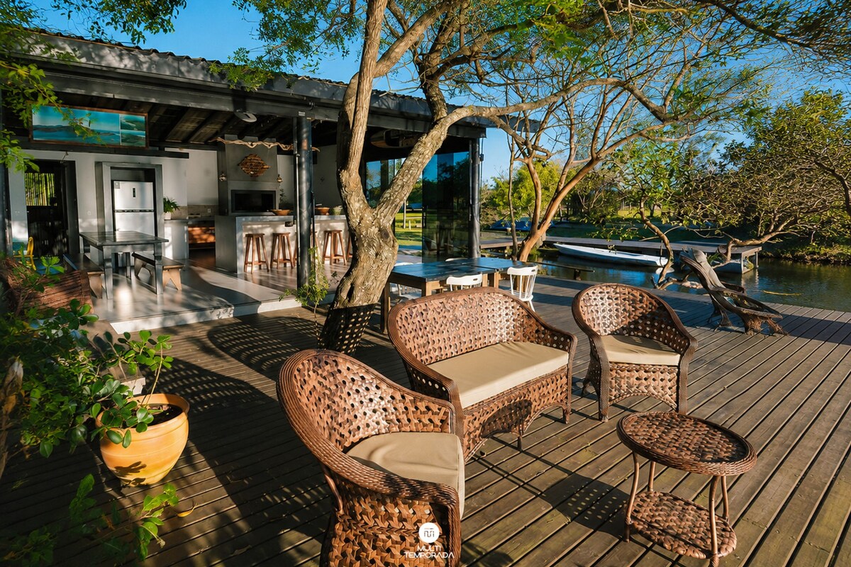 An outdoor deck with wicker furniture, a bar area, and a view of a body of water.