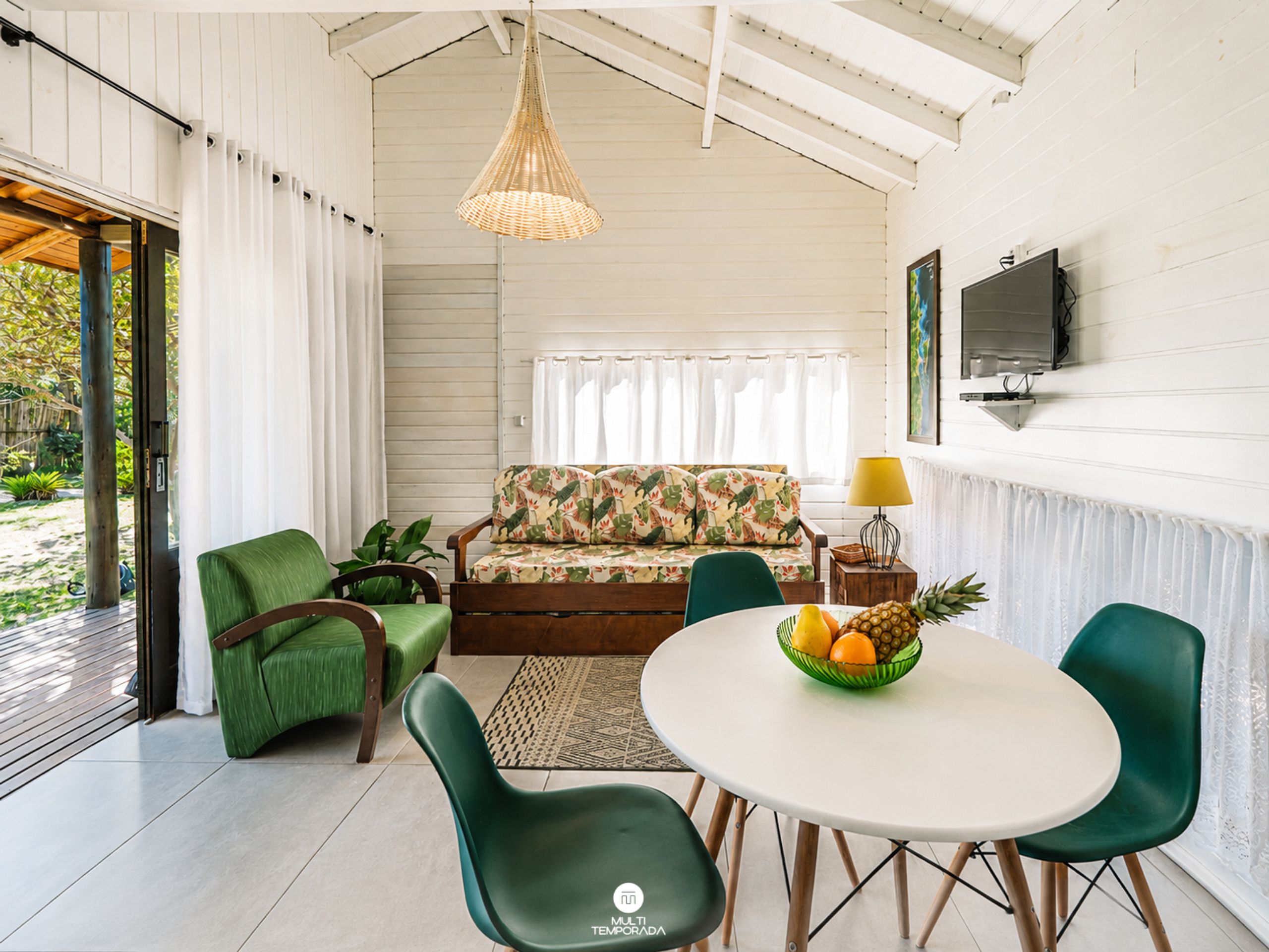 Una sala de estar moderna con un sofá, sillas, una mesa de comedor con fruta y un televisor en la pared.