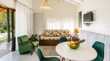 Una sala de estar moderna con un sofá, sillas, una mesa de comedor con fruta y un televisor en la pared.