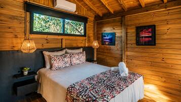 Quarto de cabana de madeira com cama, duas luminárias fixadas na parede, janela com vista e ar condicionado instalado.