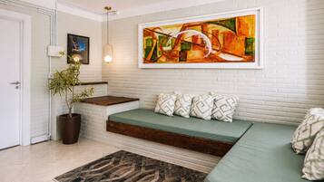Uma sala de estar moderna com parede de tijolos brancos, um sofá verde com almofadas estampadas, um banco de madeira, uma planta em vaso e uma pintura abstrata grande.
