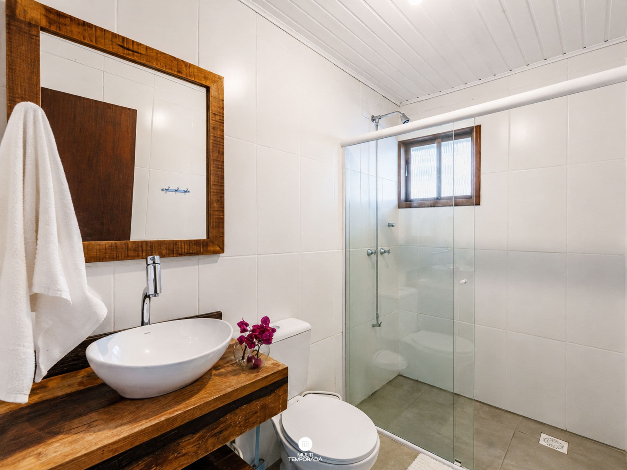 A bathroom with a wooden vanity, a white sink, a toilet, and a glass-enclosed shower.