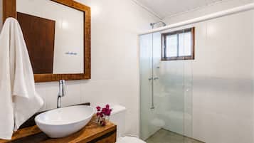 A bathroom with a wooden vanity, a white sink, a toilet, and a glass-enclosed shower.