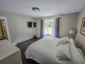 A bedroom with a bed, a television mounted on the wall, a window with curtains, and a bedside lamp. - Oceanfront house close to Acadia National Park! (Ellsworth)