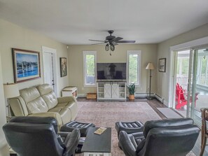 A living room with a sofa, chairs, a TV, a ceiling fan, and a view through a glass door. - Oceanfront house close to Acadia National Park! (Ellsworth)