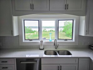 A kitchen with a double sink, a window with a view of greenery, and a dish soap bottle. - Oceanfront house close to Acadia National Park! (Ellsworth)