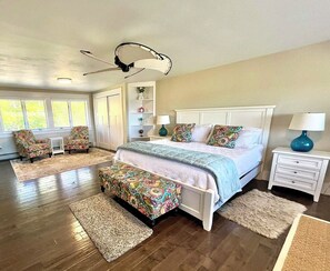 A bedroom with a large bed, two chairs, a ceiling fan, and a nightstand with a lamp. - Oceanfront house close to Acadia National Park! (Ellsworth)