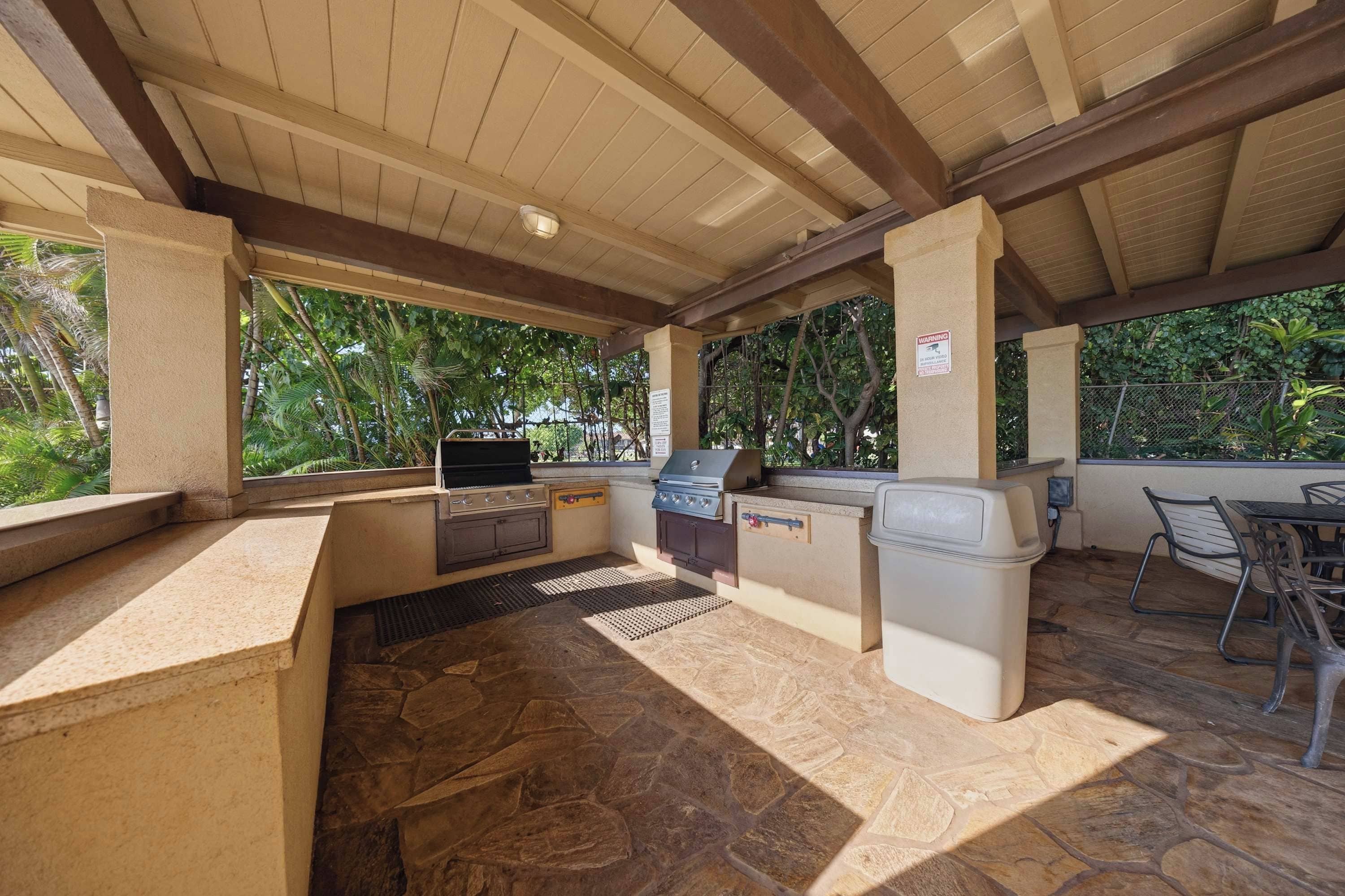 Une terrasse extérieure avec un sol en pierre, un barbecue et un espace détente avec des chaises.