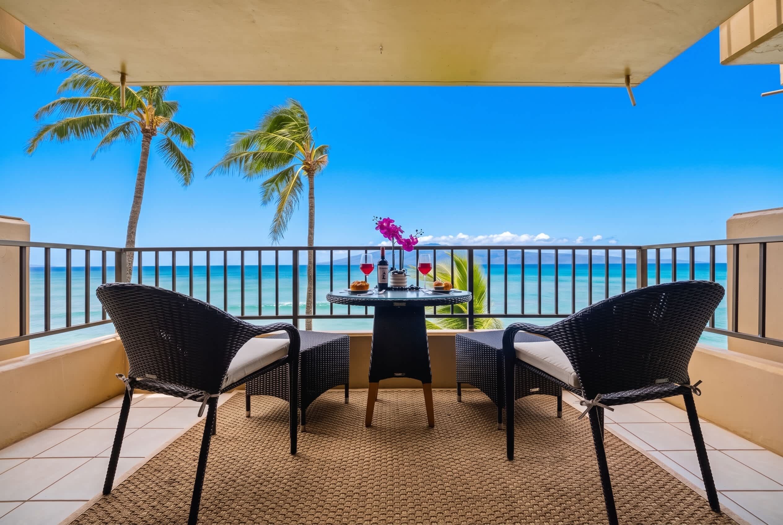 Ein Balkon mit Tisch und Stühlen mit Blick auf einen Strand, an dem Palmen und das Meer zu sehen sind.