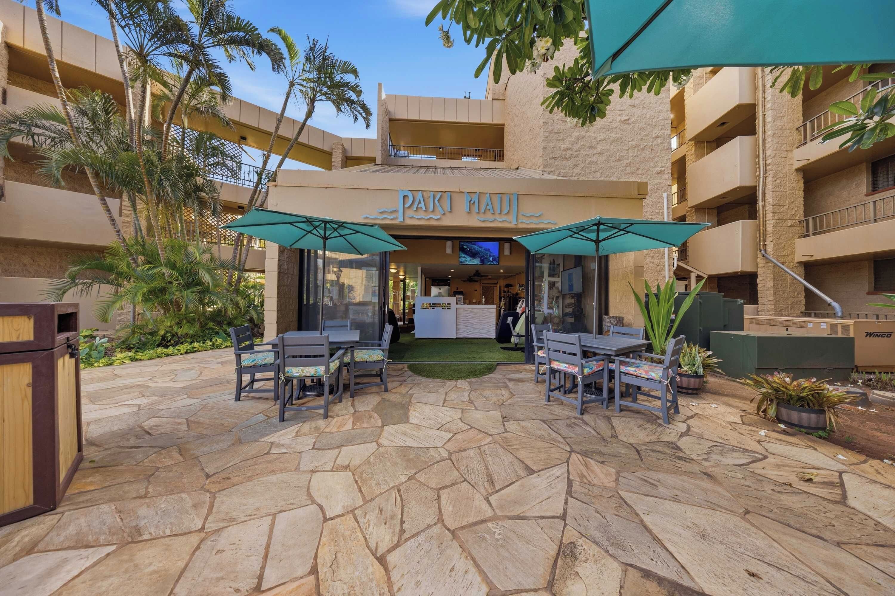 A hotel courtyard with outdoor seating, palm trees, and a sign for 'PAK MAUI'.