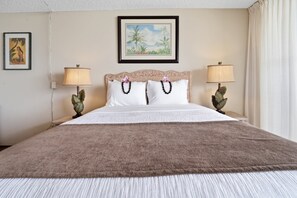 A hotel room with a large bed, two bedside lamps, a framed painting on the wall, and a window with curtains.
