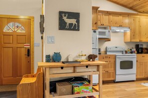 A kitchen with wooden cabinets, a microwave, an oven, and a table with a laptop and decorative items. - Family-Friendly Lake Wenatchee Retreat with Private Hot Tub & Large Deck (Leavenworth)