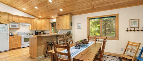 A modern kitchen with wooden cabinets, a central island, and a dining area with a table and chairs.
