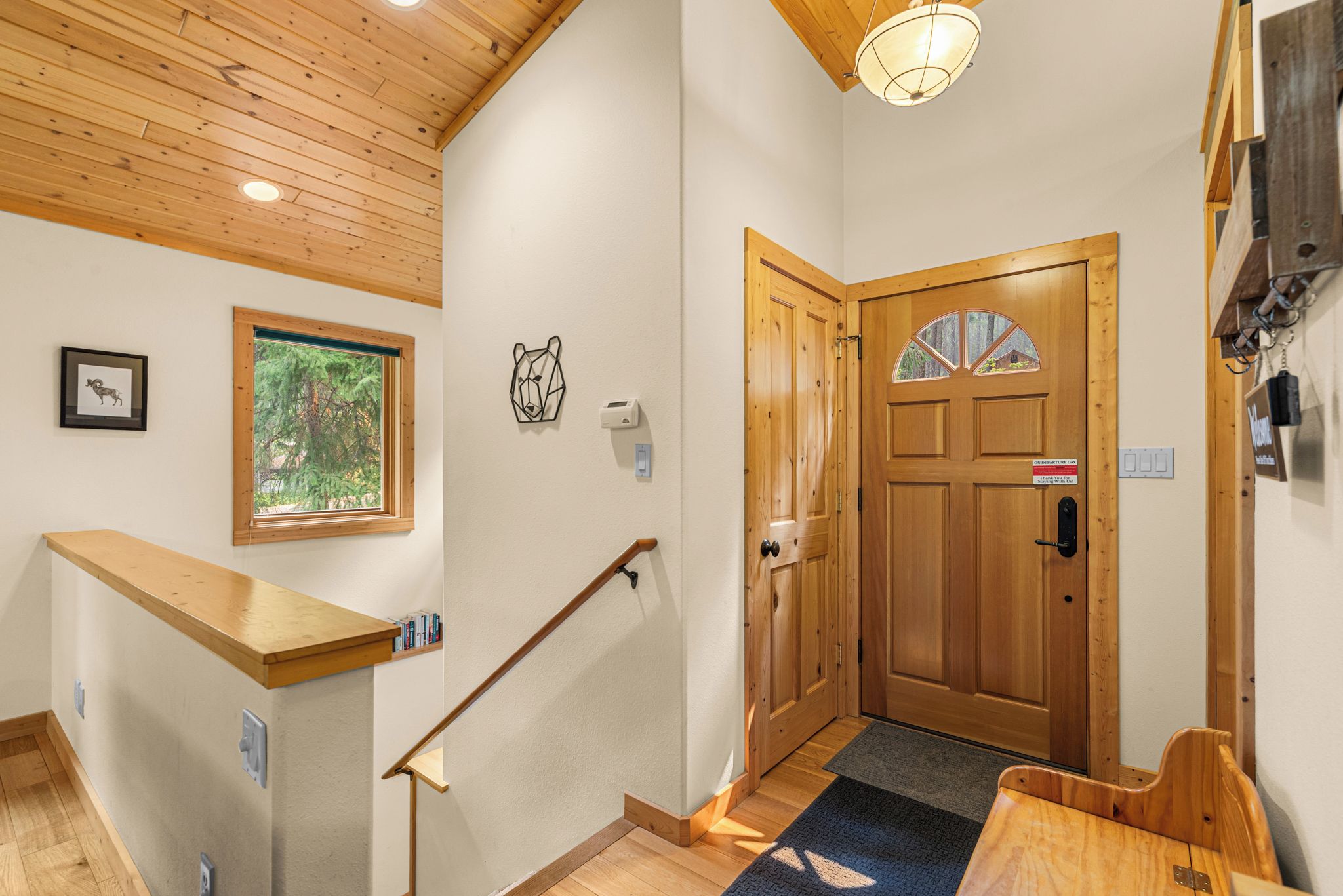 A wooden staircase with a handrail, a door with a window, and a wall-mounted light fixture.