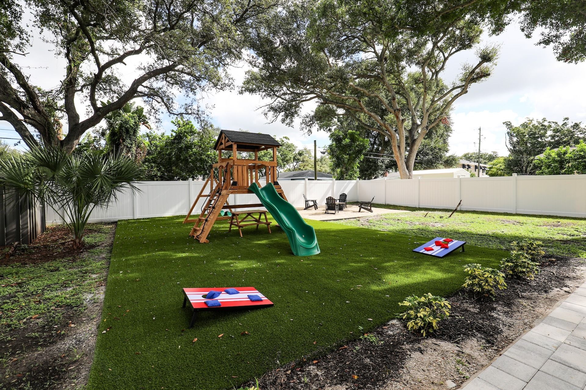 A backyard with a wooden play structure, a green slide, and a red and blue mat.