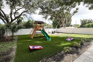 A backyard with a wooden play structure, a green slide, and a red and blue mat. - Beach, Bark and Bonfire - Spa/Firepit Home - Largo (Largo)