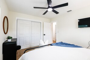 A bedroom with a bed, a ceiling fan, a TV mounted on the wall, and a door leading to another room. - Beach, Bark and Bonfire - Spa/Firepit Home - Largo (Largo)