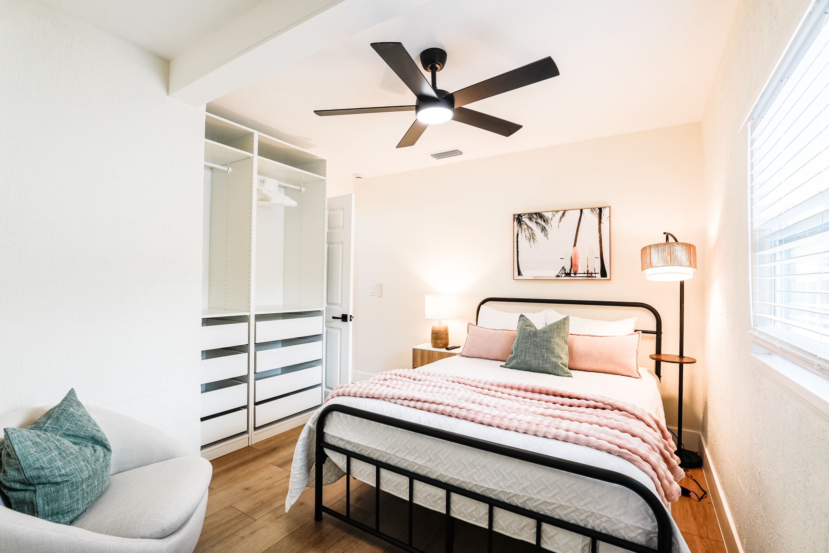 A bedroom with a bed, bedside lamps, a ceiling fan, a wardrobe, and a window.