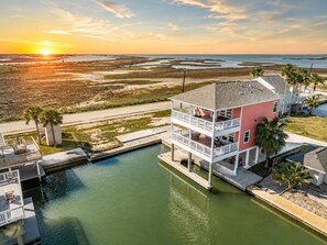 A waterfront property with a two-story building, a dock, and a view of the sunset over the water. - Jamaica Beach | Bayfront | Hot Tub | Kayaks (Jamaica Beach)