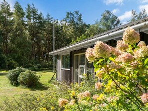 Ein Haus mit überdachter Veranda, umgeben von einem üppigen Garten und hohen Bäumen.
