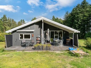 Eine kleine Holzhütte mit einer Terrasse, Sitzgelegenheit im Freien und Grillplatz.