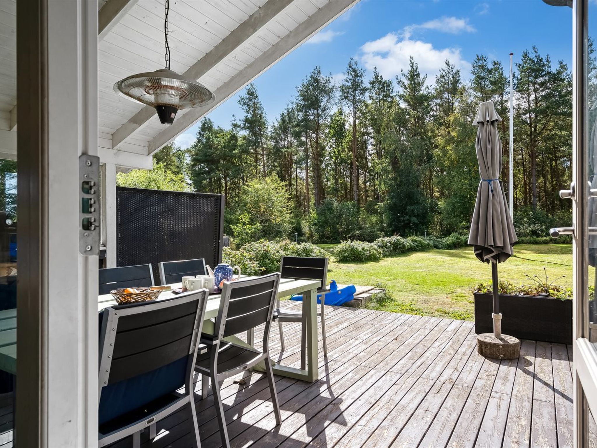An outdoor deck with a table and chairs, a fan, and a view of a forest.