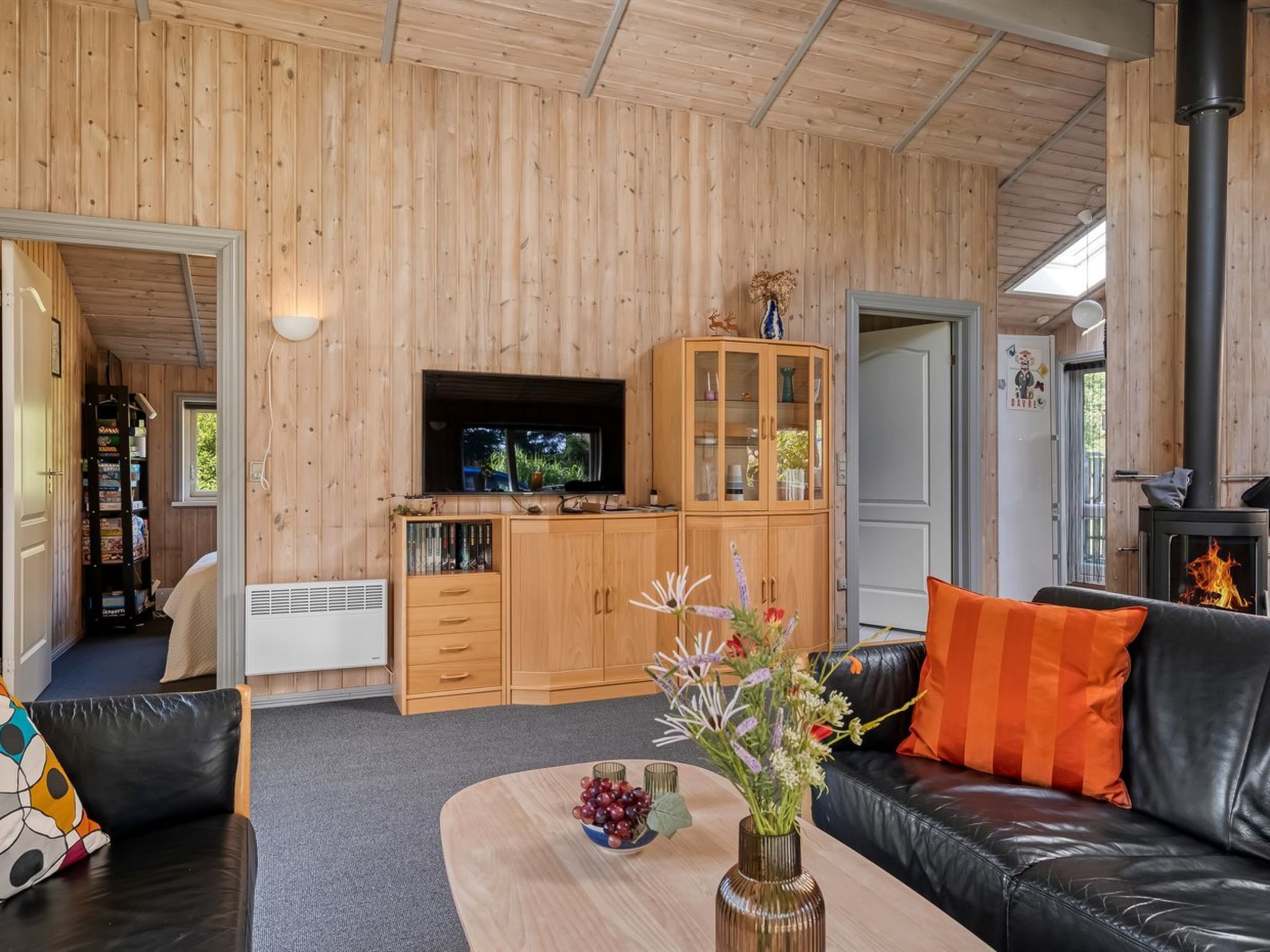 A cozy living room with a fireplace, wooden cabinets, a television, and a sofa with cushions.