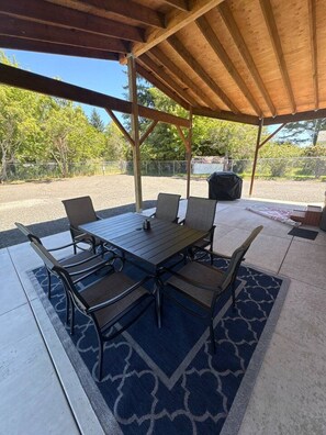 An outdoor patio with a wooden table and chairs, surrounded by a patterned rug. - Coastal Retreat w/ Hot Tub Near Beach (Coos Bay)