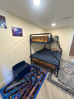 A bunk bed with a wooden headboard, a blue mattress, and a black metal frame. There is a colorful race track rug on the floor.
