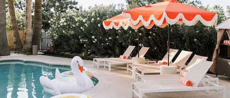 A pool area with lounge chairs, a swan float, and a decorative umbrella.