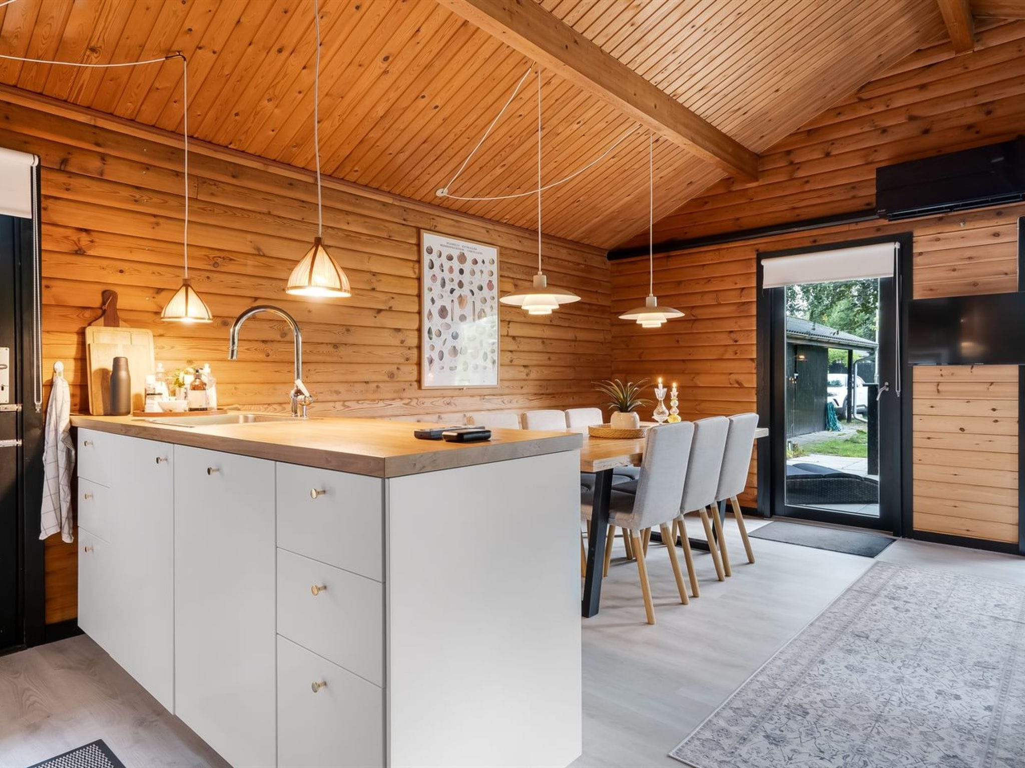 Une cuisine moderne dotée d’un îlot central, de luminaires suspendus et offrant une vue sur l’extérieur.