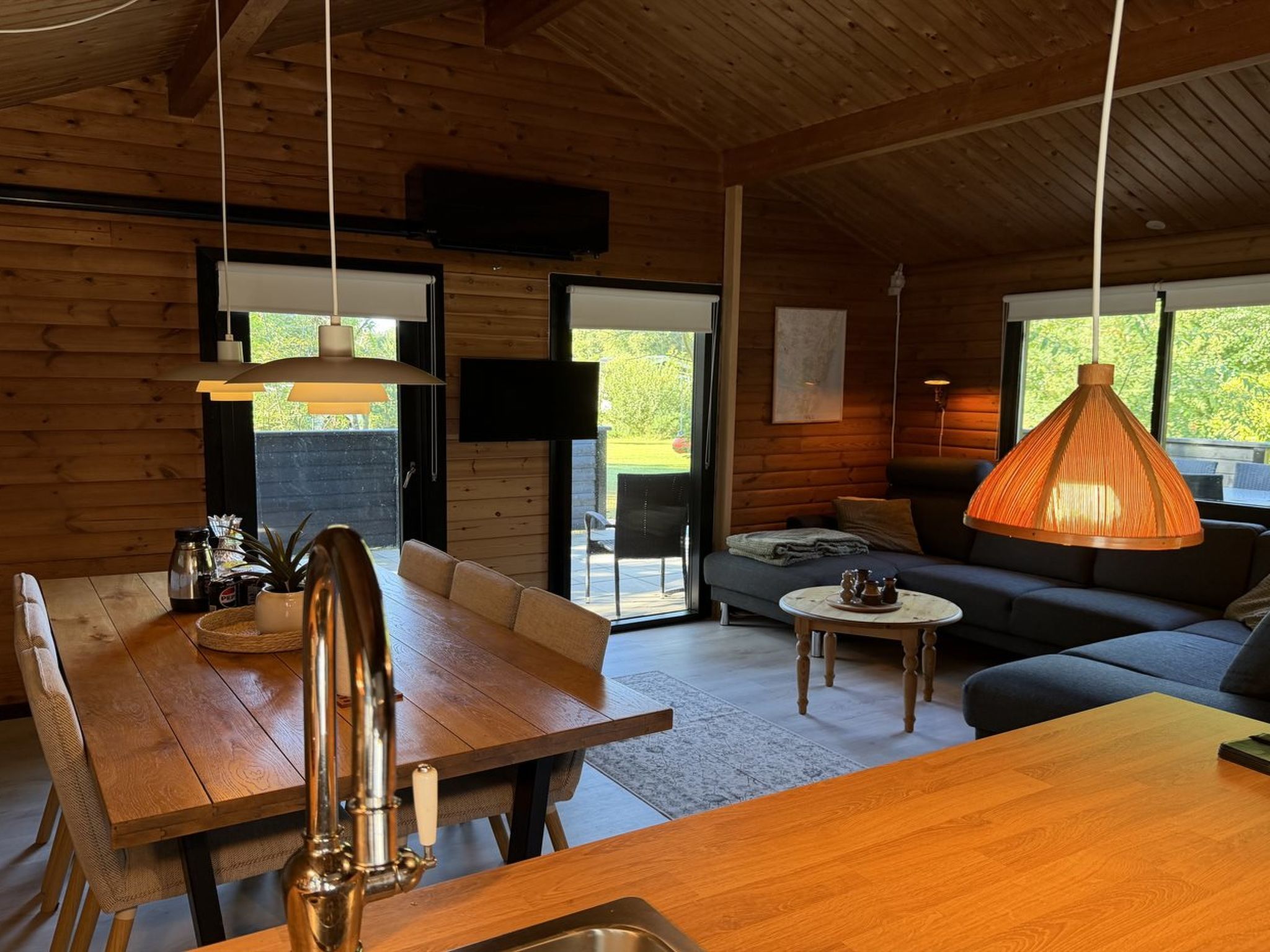 Interior acollidor d'una cabana amb una taula de dinar de fusta, un sofà i un llum penjant.