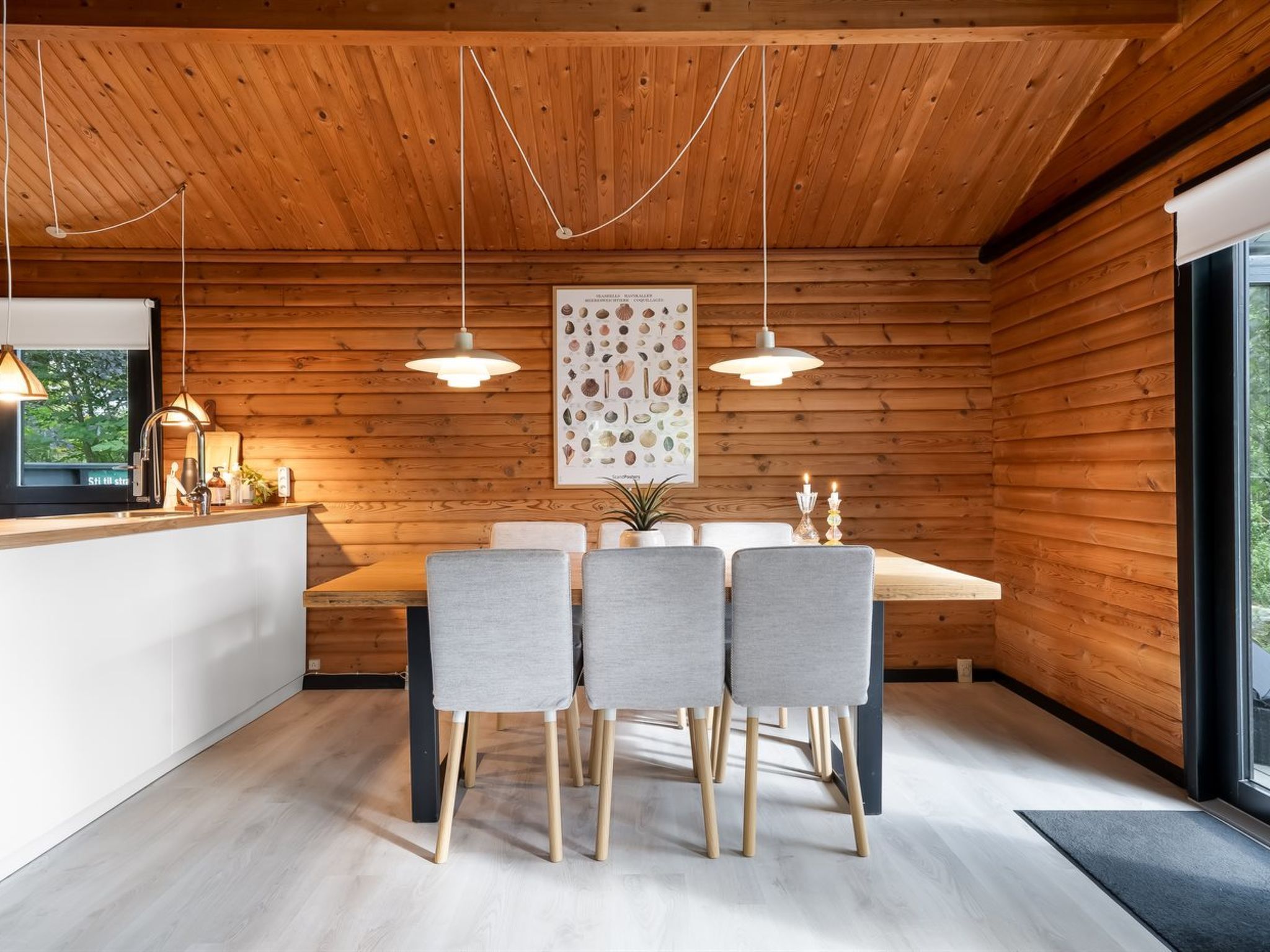 Une cuisine moderne avec des murs en bois, une table à manger entourée de quatre chaises, des luminaires suspendus et un grand tableau encadré au mur.