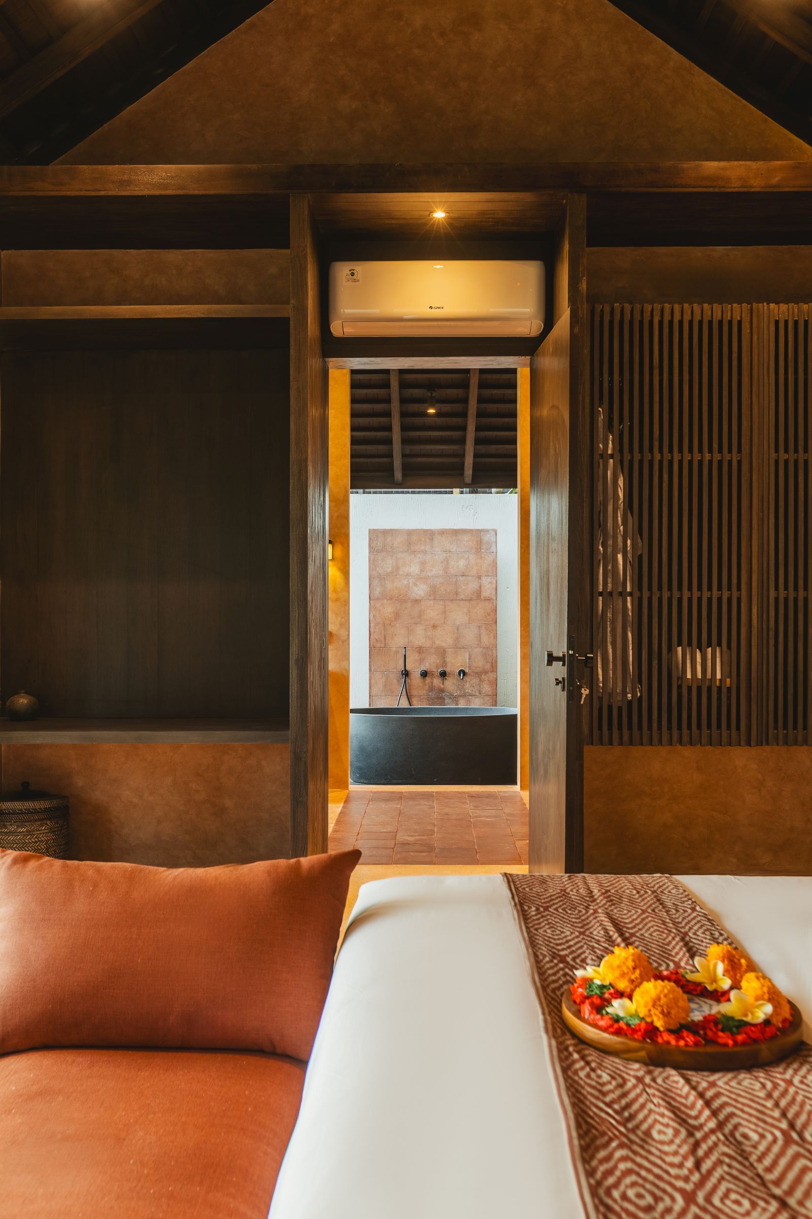 Habitación de hotel con cama, una pequeña mesa con una bandeja de frutas, aire acondicionado en la pared y vista a un área de spa.