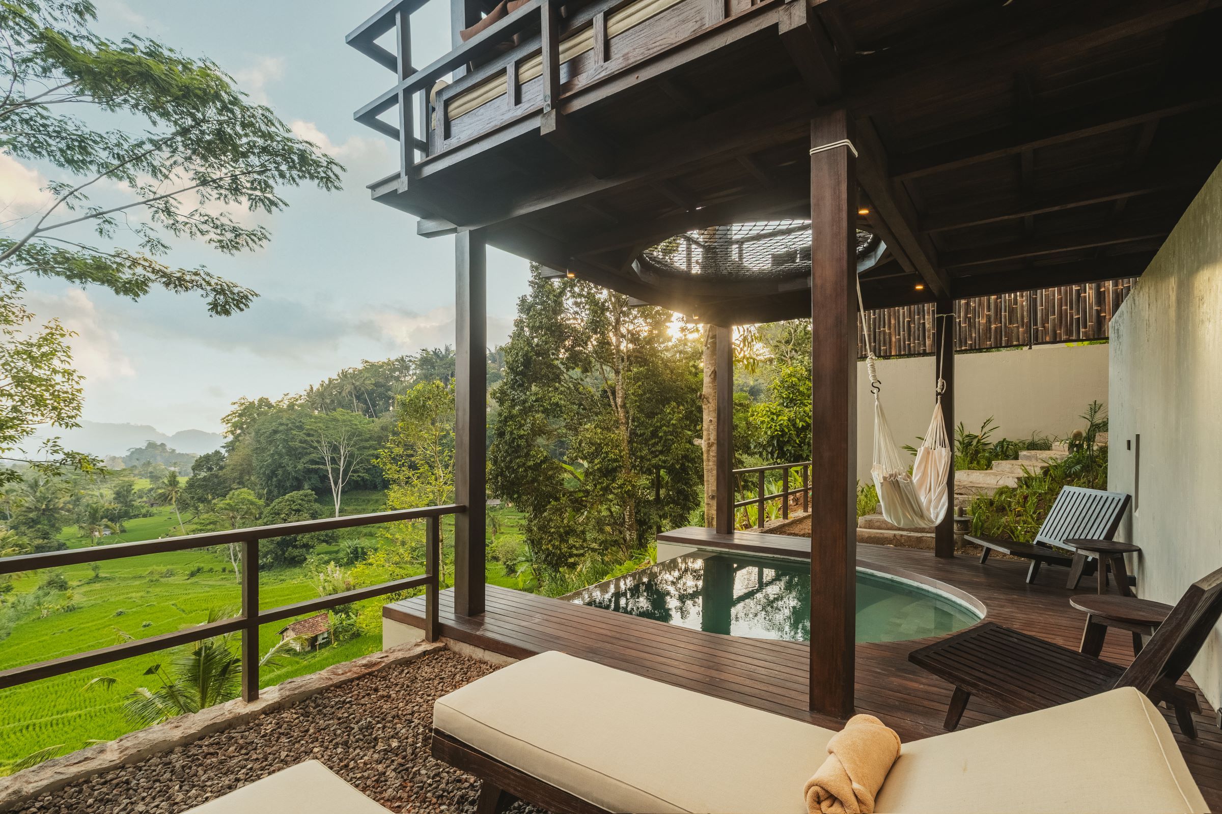 Zona junto a la piscina con vistas a un paisaje exuberante, una terraza de madera y una silla de descanso.