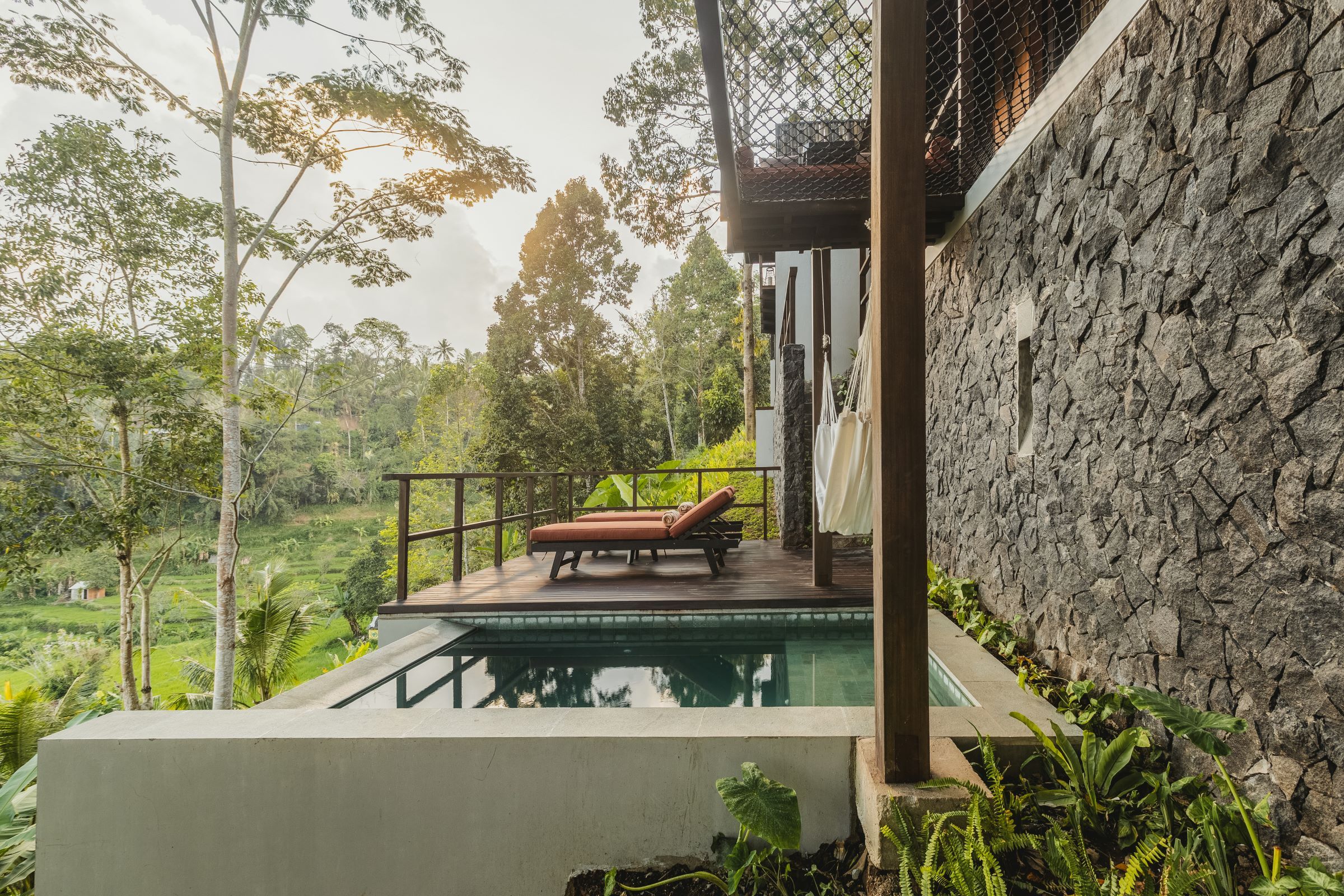 A poolside area with a lounge chair and a stone wall.