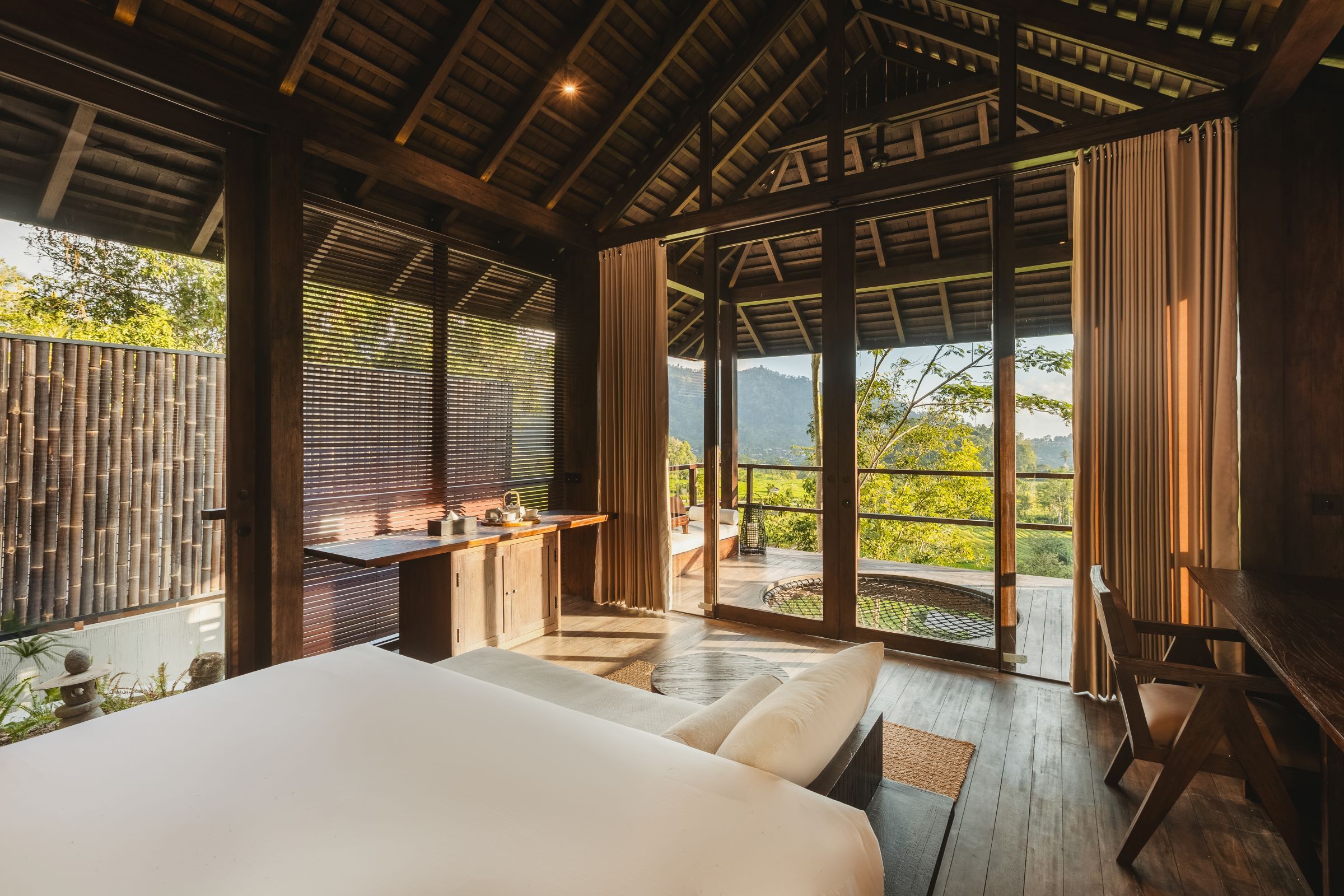 Un dormitorio con una cama grande, un escritorio de madera y vistas a un paisaje montañoso a través de amplios ventanales.