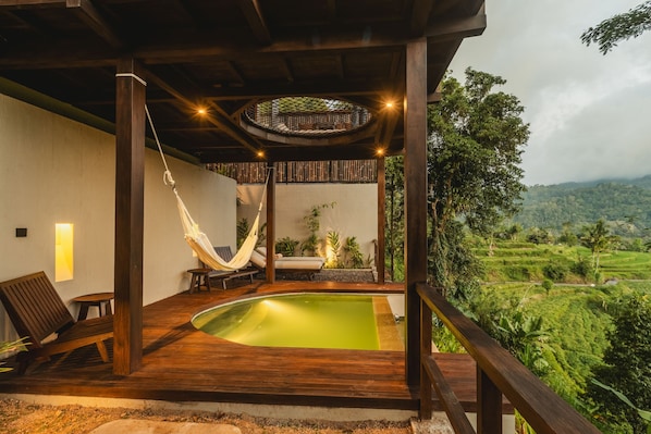 Una terraza de madera con piscina, sillas de descanso y una hamaca.