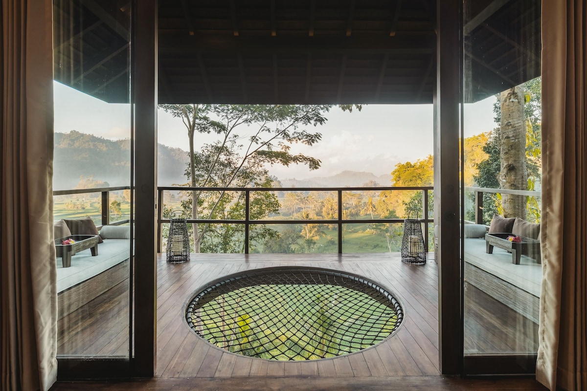 Un jacuzzi circular con cubierta de red, rodeado de piso de madera, con vista a un paisaje pintoresco con árboles y colinas.