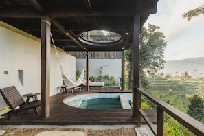 Una terraza de madera con piscina, sillas de descanso y una hamaca colgante.