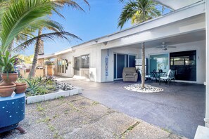 Ein modernes Haus mit überdachter Terrasse, Sitzgelegenheiten im Freien und einem kleinen Garten.